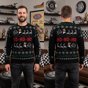 A man modeling a black Christmas sweater in a garage-like setting, shown from both the front and back. The sweater features a holiday print with reindeer, snowflakes, and the text 'HO-HO-HO' in red, with green and white accents.