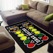 A black rectangular area rug with a drag racing theme, featuring white text and colorful traffic light shapes, shown on a light wood floor in a living room setting next to a brown sectional sofa.