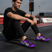 Man sitting on a race track wearing purple sneakers with a brand logo.