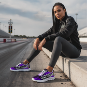 Woman sitting on a race track wearing black jacket, gray leggings, and purple sneakers.