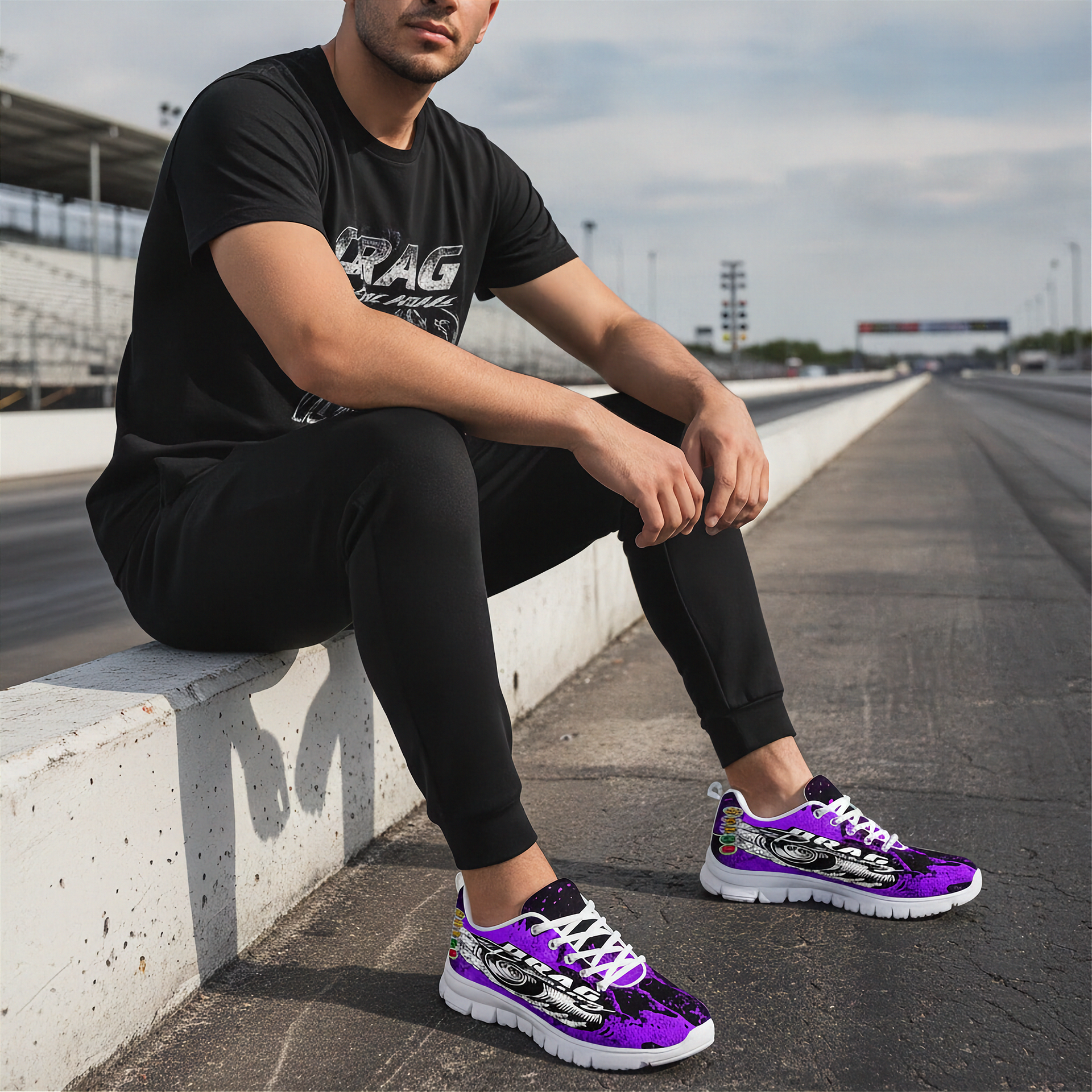 Person wearing black t-shirt and pants with purple sneakers sitting on a track.