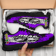 Purple and black sneakers with 'Drag' text held by a hand, displayed in an open cardboard box.