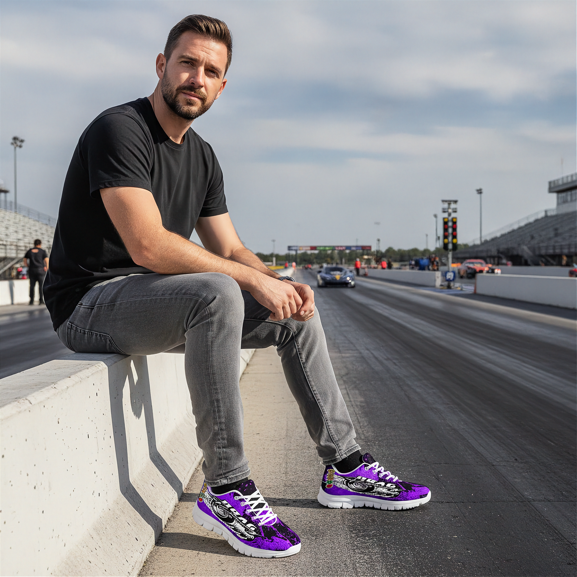 Man sitting on a barrier at a race track wearing black and purple sneakers.