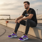 Man sitting on a concrete ledge wearing black t-shirt, dark pants, and purple sneakers with a track in the background.