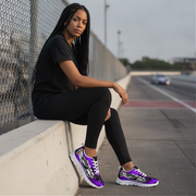 Woman sitting on a concrete barrier by a road wearing black athletic wear and purple sneakers.