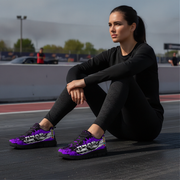 Woman sitting on a track wearing black outfit and purple sneakers with white designs.