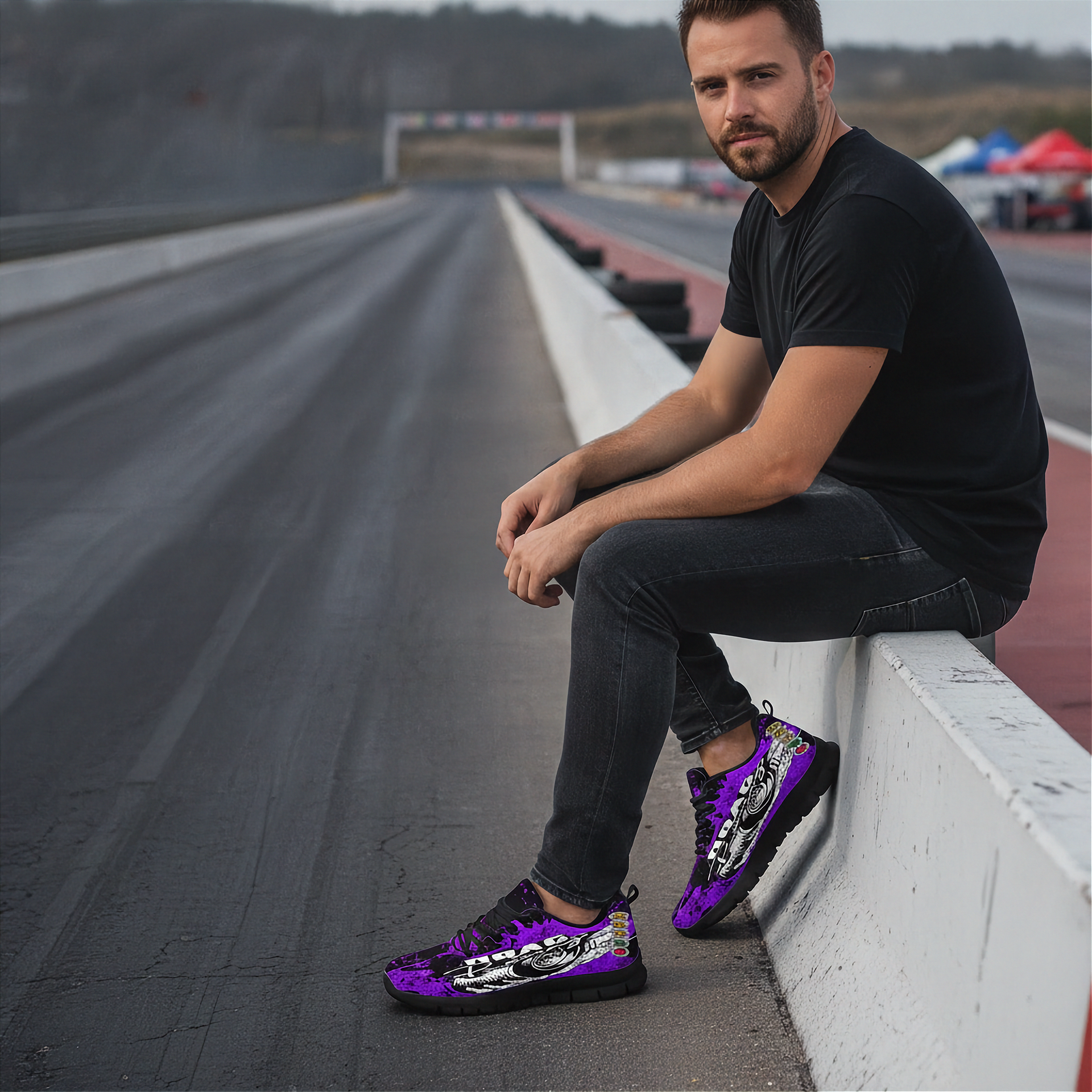 Man sitting on a race track wall wearing purple sneakers with black patterns.