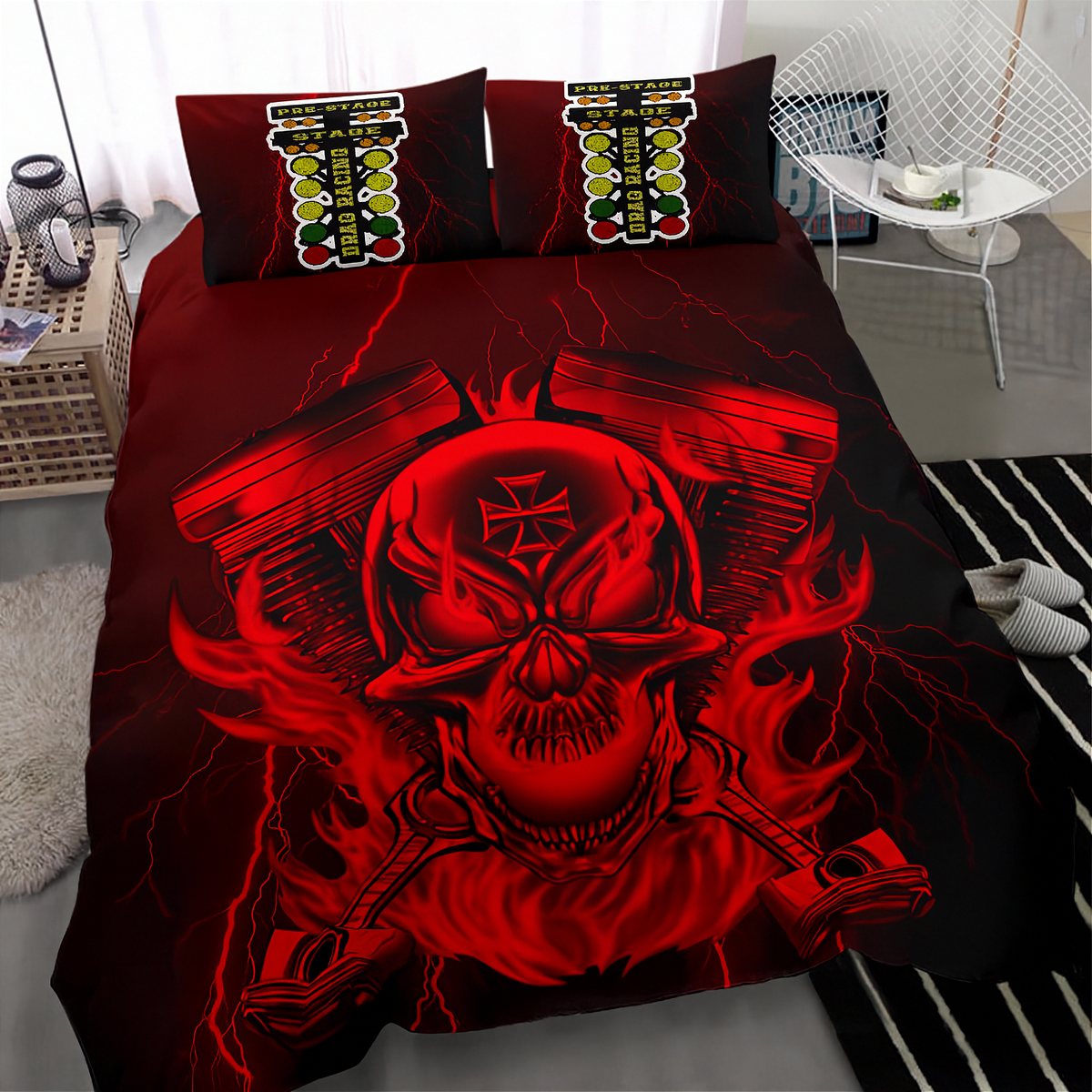 A bed dressed in a black and red graphic bedding set featuring a large skull with an iron cross on its forehead, flanked by engine blocks and lightning effects. Two matching pillowcases are visible at the head of the bed, and the room setting includes a white chair, bedside table, and rug.