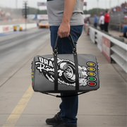 A person standing on a racetrack holds a gray duffel bag with a large black-and-white drag racer graphic, including the words 'Drag Racer' and colored light buttons on the side.