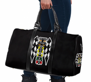 A black duffel bag with racing-themed graphics, held by a person wearing blue jeans and black boots against a white background.