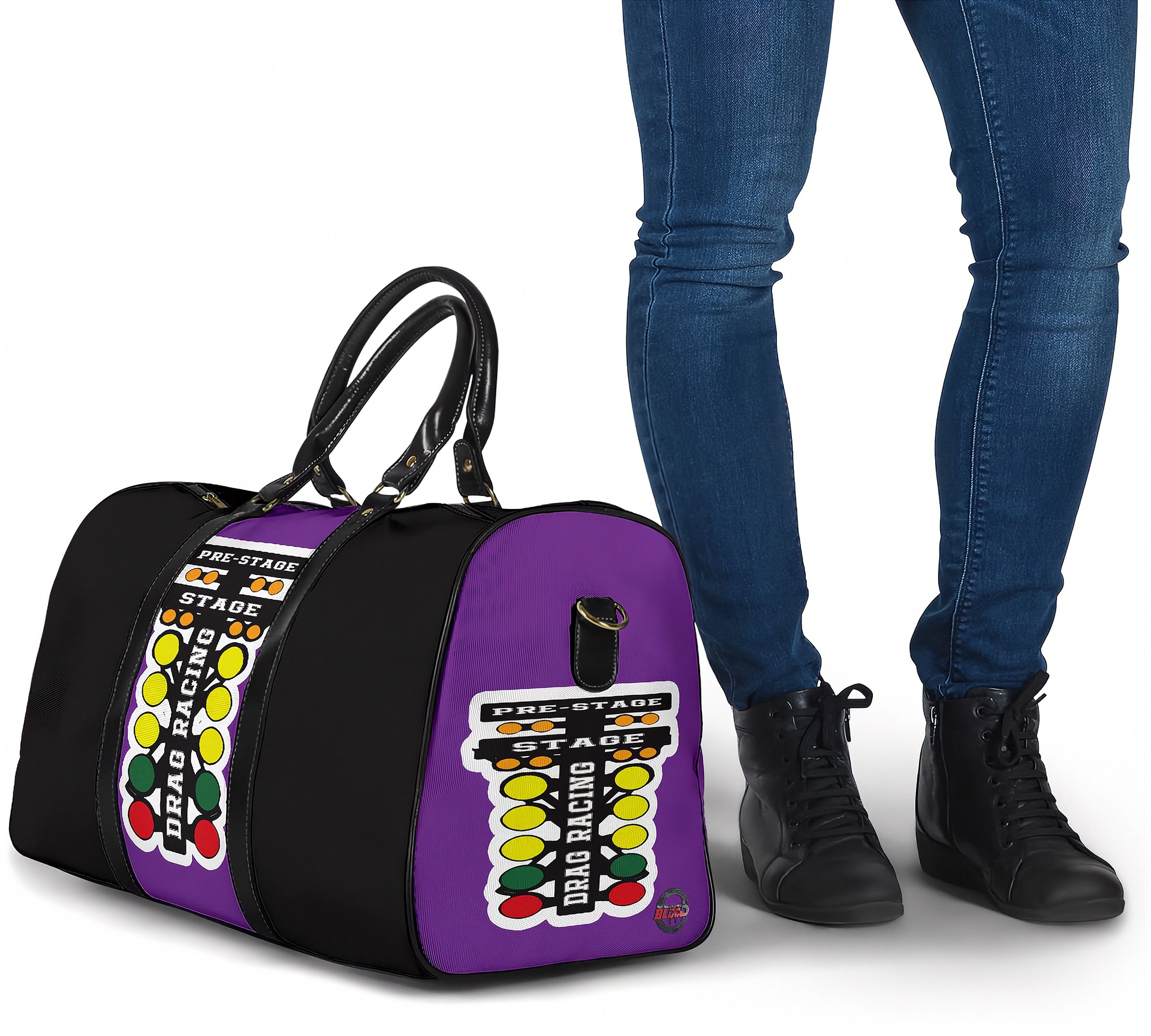 A purple and black duffel bag with a bold graphic print featuring the words 'FUEL STATION' and colorful circular icons, shown next to a person wearing blue jeans and black boots on a white background.