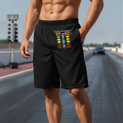 A man wearing black athletic shorts with a colorful 'Pit Stop' traffic light graphic on the front, standing on a racetrack.