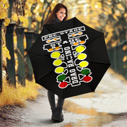 A woman holding a black umbrella in an outdoor autumn setting with yellow foliage and a wet path. The umbrella features a white, yellow, green, and red drag racing flag graphic with the text 'PRE-STAGE', 'STAGE', and 'DRAG RACING'.