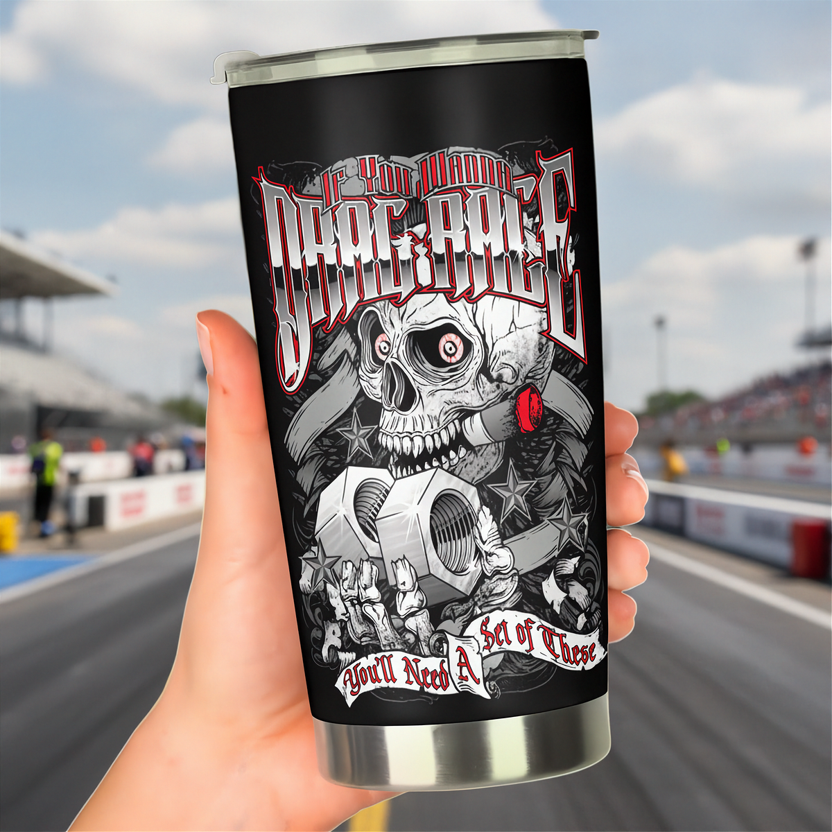 A hand holds a stainless steel travel tumbler with a black background and a detailed graphic of a skull, gears, and the text 'If You Wanna To Drag Race You'll Need A Set of These' against a blurred racetrack background.