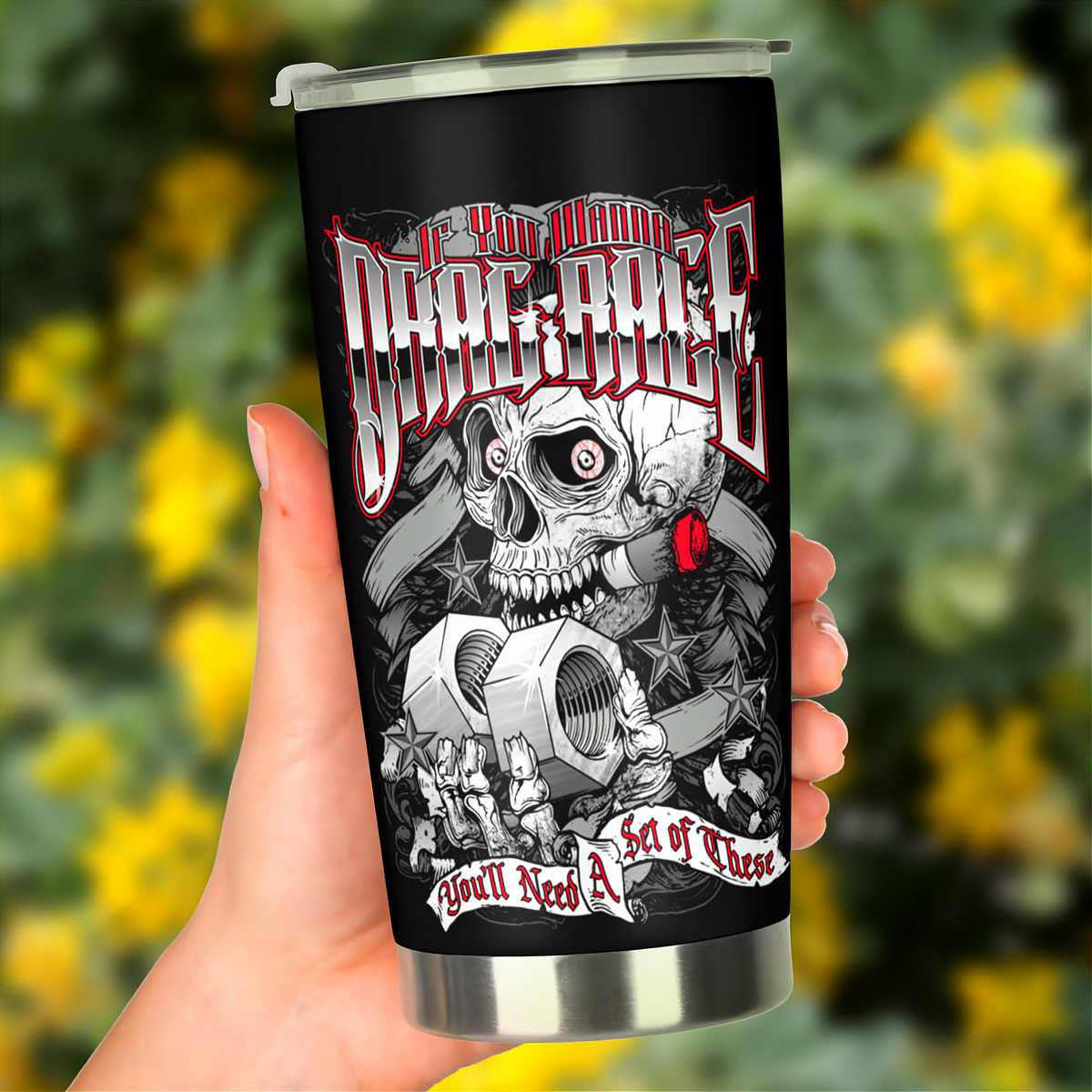 A hand holds a black insulated travel tumbler with a clear lid. The tumbler features a detailed graphic of a skull smoking a red joint, with the text 'If You Wanna To Drag Race You'll Need A Set of These' in stylized lettering.