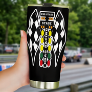 A hand holding a black travel tumbler with a racing-themed graphic that includes checkered flags, the words 'PRE-STAGE', 'STAGE', and 'DRAG RACING', against a blurred racetrack background.
