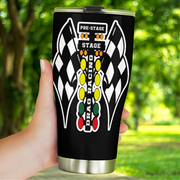 A hand holding a black insulated travel tumbler with a stainless steel lid and base. The tumbler features a white and black checkered wing graphic and a vertical 'DRAG RACING' graphic with traffic light colors (yellow, green, red) on a blurred green outdoor background.