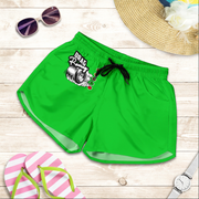 Bright green athletic shorts with a black drawstring and a 'Drag Racing' graphic on the left leg, styled in a flat lay on a light wood background with sunglasses, a straw hat, flip-flops, and a watch.