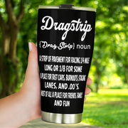 Hand holding a black Dragstrip Noun Tumbler outdoors against a leafy green background.