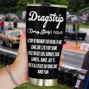 Black Dragstrip definition tumbler held near the starting line, with race cars and drag tree lights behind it.