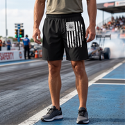 A man standing on a drag racing track wearing black athletic shorts with a white vertical American flag graphic and the word 'EAT SLEEP DRAG RACING REPEAT' printed down the side.