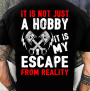 A person wearing a black T-shirt shown from the back, with a large distressed graphic and text reading “IT IS NOT JUST A HOBBY IT IS MY ESCAPE FROM REALITY” in red and white, plus crossed wrenches and lightning bolt icons.