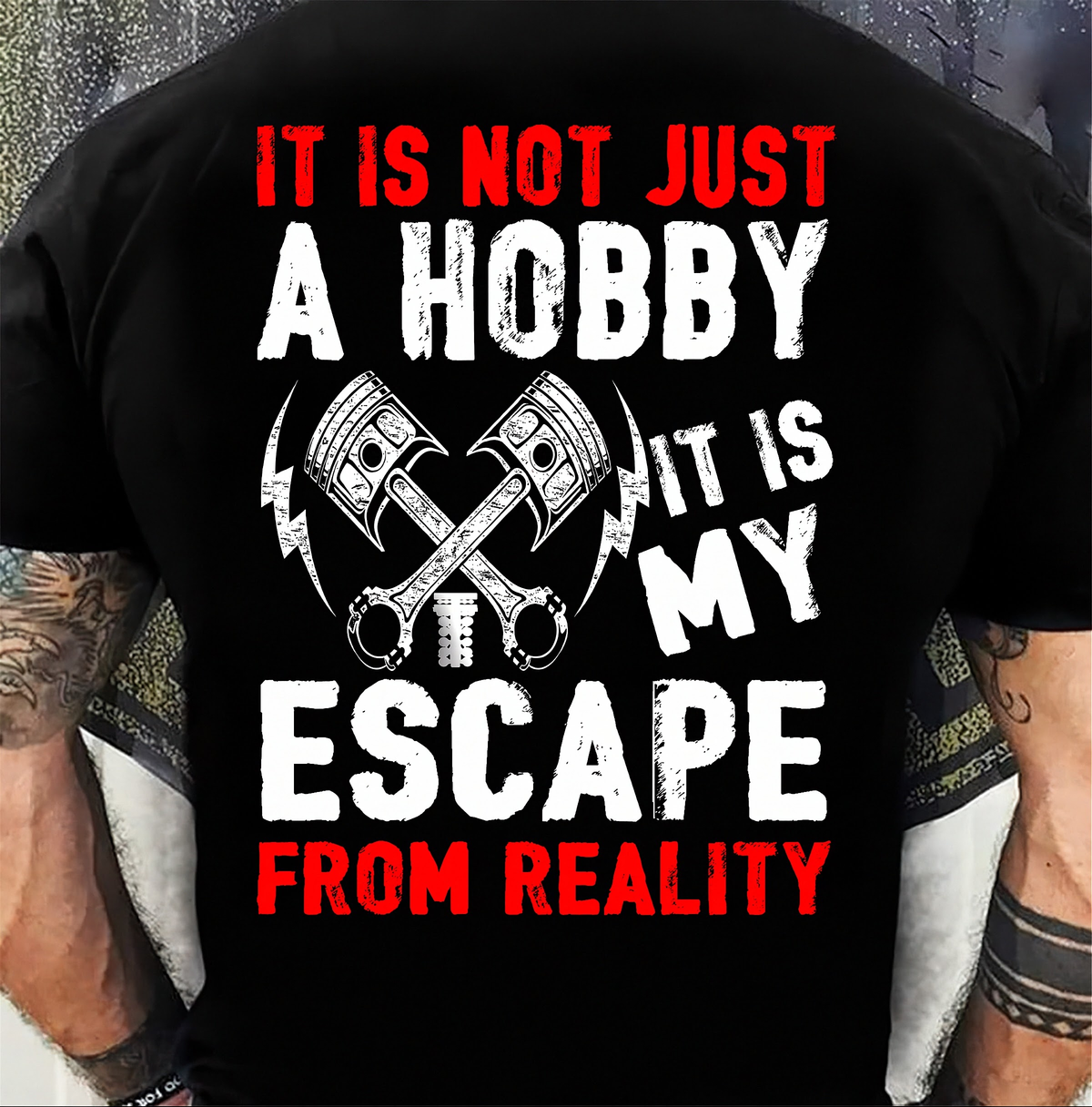 A person wearing a black T-shirt shown from the back, with a large distressed graphic and text reading “IT IS NOT JUST A HOBBY IT IS MY ESCAPE FROM REALITY” in red and white, plus crossed wrenches and lightning bolt icons.