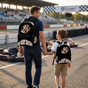 A young kart racer aged 8 to 12 standing in an outdoor track pit lane next to a sleek orange racing kart, wearing a custom orange go-kart track backpack with thick black padded shoulder straps while holding a racing helmet.