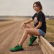 Woman sitting on a track wearing black t-shirt, denim shorts, and green checkered shoes.
