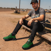 Man sitting on a wooden bench wearing green checkered shoes in an outdoor setting.