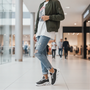 Woman wearing a green bomber jacket, white t-shirt, blue jeans, and checkered sneakers in a mall.