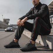 Man sitting on a race track wearing black and red athletic gear with checkered shoes.