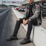 Man sitting on a race track wall wearing a branded jacket and checkered shoes.
