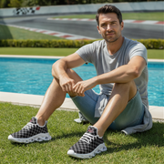Man sitting by a pool wearing checkered shoes and casual clothing.