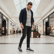 Man in a mall wearing a navy hoodie, white t-shirt, black jeans, and patterned sneakers.