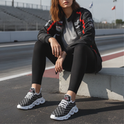 Woman sitting on a track wearing a branded jacket and checkered shoes.