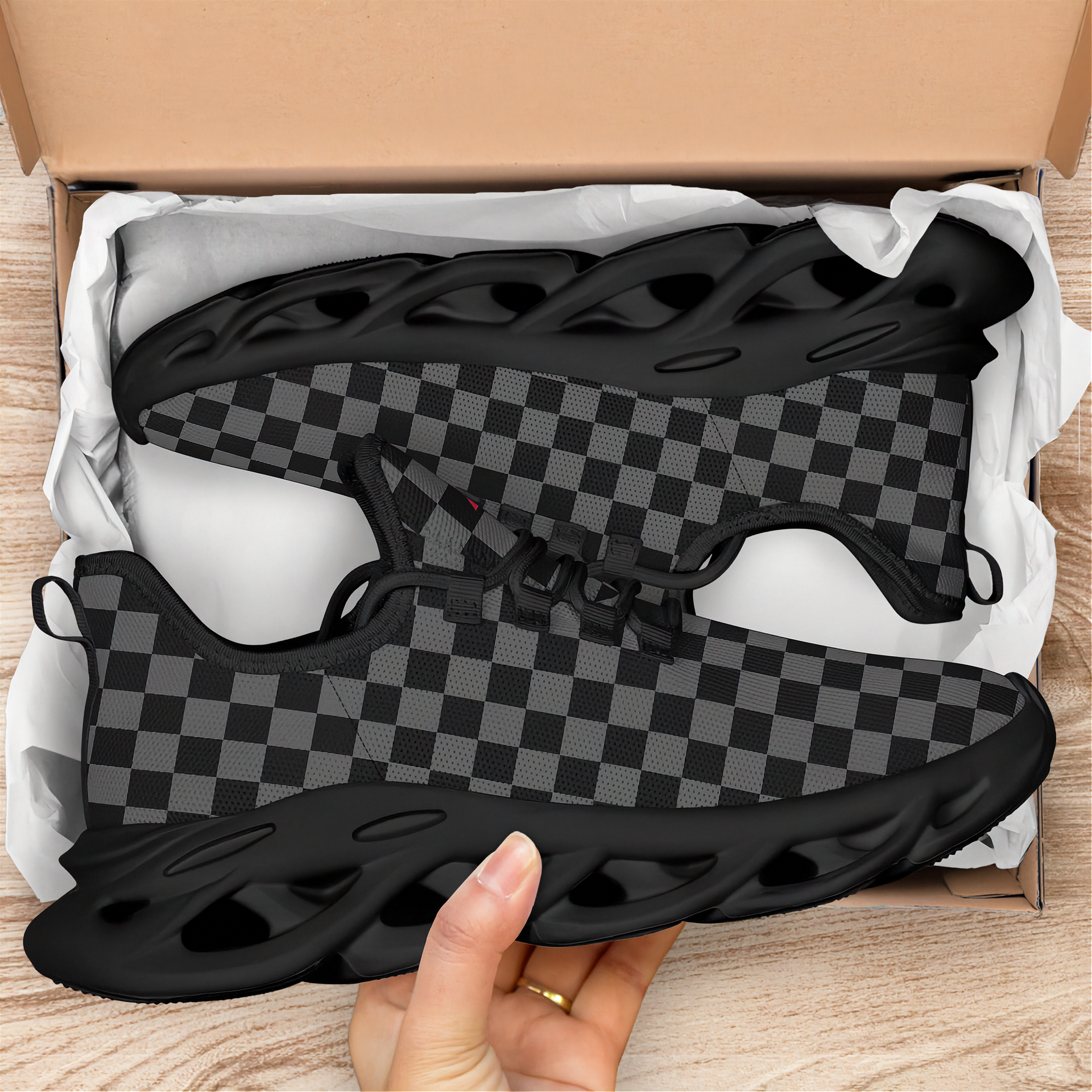 Black and gray checkered sneakers in an open cardboard box on a wooden surface.