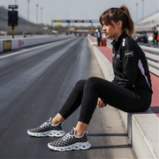 Woman sitting on a race track wearing black athletic gear and checkered shoes.