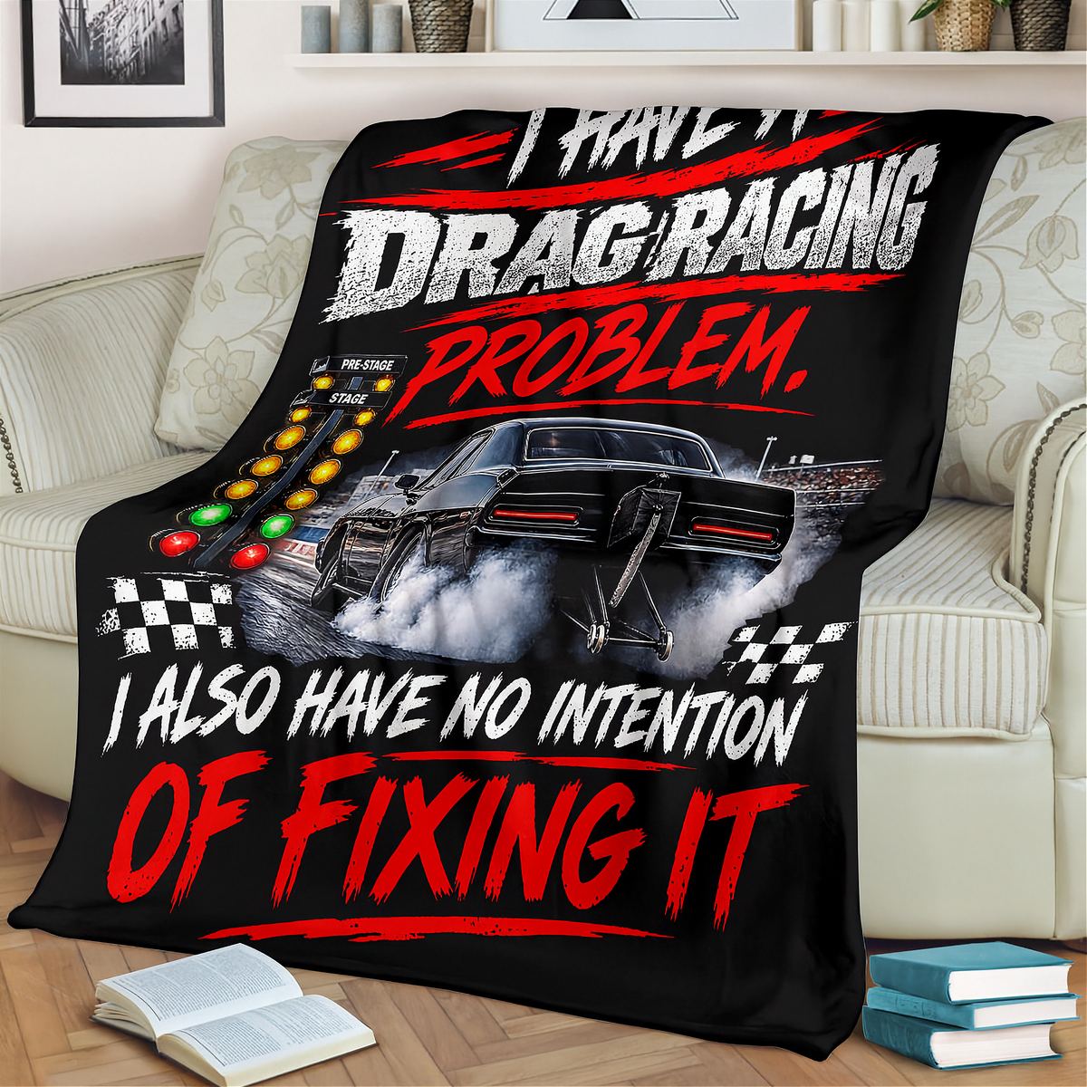 A black throw blanket featuring a drag racing graphic with the text 'I HAVE IT DRAG RACING PROBLEM. I ALSO HAVE NO INTENTION OF FIXING IT' is draped over a beige sofa in a living room setting.