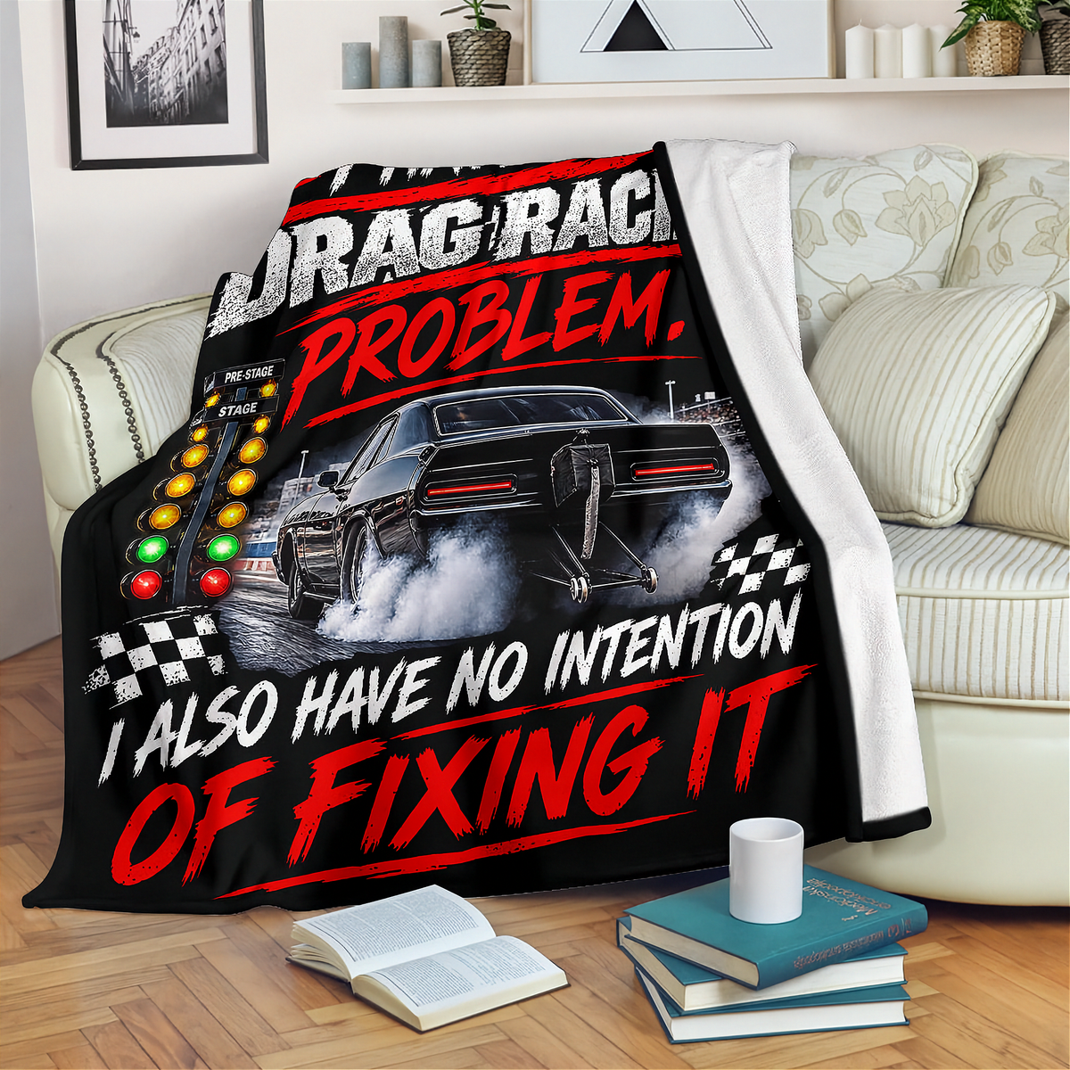 A black throw blanket with a drag racing graphic and bold text is draped over a cream sofa in a living room setting. The blanket features a black muscle car, racing lights, checkered flags, and the phrases 'DRAG RACING PROBLEM.