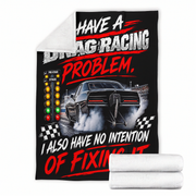 A black fleece throw blanket featuring a drag racing graphic with a black muscle car, a starting light sequence, and the text 'HAVE A DRAG RACING PROBLEM, I ALSO HAVE NO INTENTION OF FIXING IT.' A white sherpa lining is visible on the folded corner, and two rolled white blankets are shown in front on a white background.