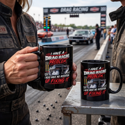 Two black ceramic mugs with a drag racing graphic design are shown in a racetrack setting. One mug is held by a person wearing a leather jacket, and the other sits on a metal table.