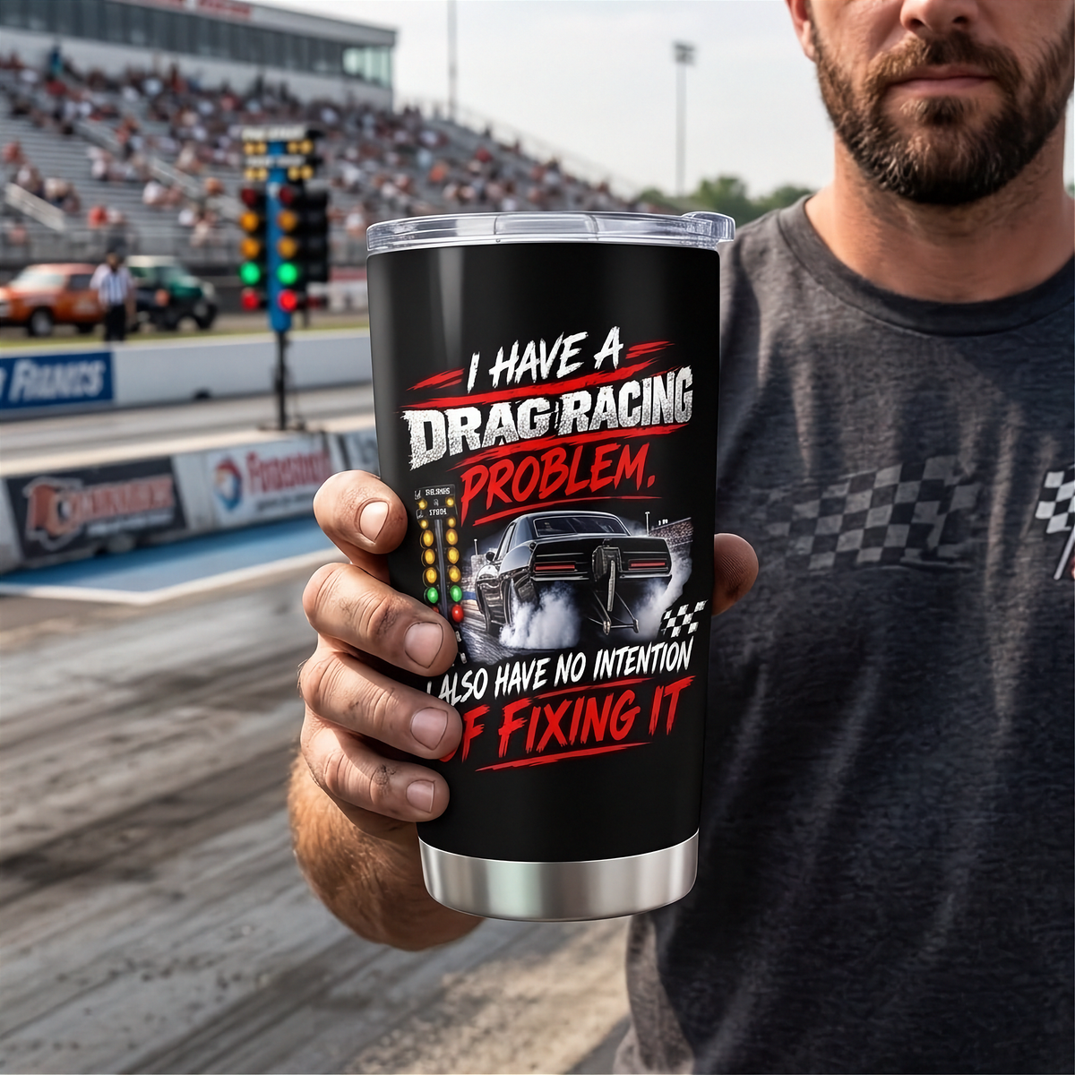 A man in a gray t-shirt holds up a black insulated tumbler with a clear lid. The tumbler features a graphic of a drag racing car and the text 'I HAVE A DRAG RACING PROBLEM, ALSO HAVE NO INTENTION OF FIXING IT' in white and red.