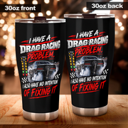 Two 30oz black insulated tumblers shown side by side on a wooden surface with a blurred warm bokeh background. The left tumbler shows the front design and the right tumbler shows the back design.