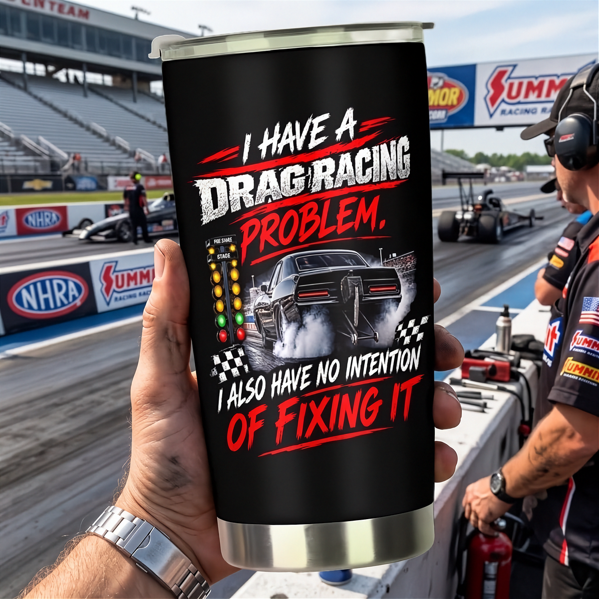 A hand holds a black insulated tumbler with a silver lid and base, printed with a drag racing graphic and the text 'I HAVE A DRAG RACING PROBLEM. I ALSO HAVE NO INTENTION OF FIXING IT.