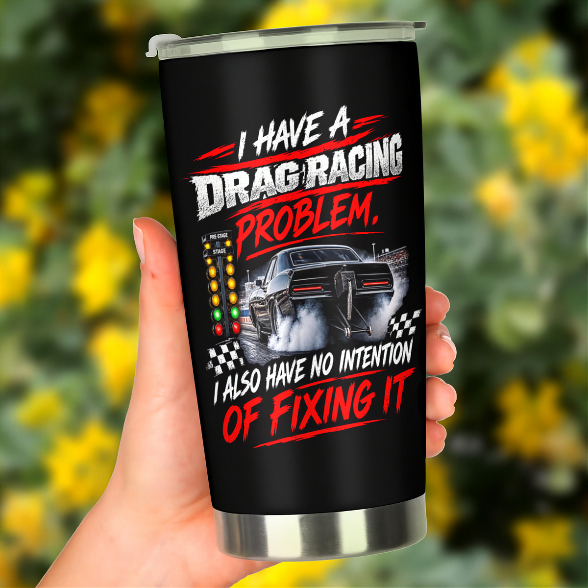 A hand holding a black insulated travel tumbler with a silver lid and base, featuring a drag racing graphic and the text 'I HAVE A DRAG RACING PROBLEM. I ALSO HAVE NO INTENTION OF FIXING IT.