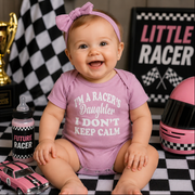 Baby holding a racing-themed blanket with a car and checkered flags design at a race track.
