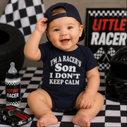 Baby wearing a navy blue onesie with text, sitting on a checkered floor with racing-themed decor.