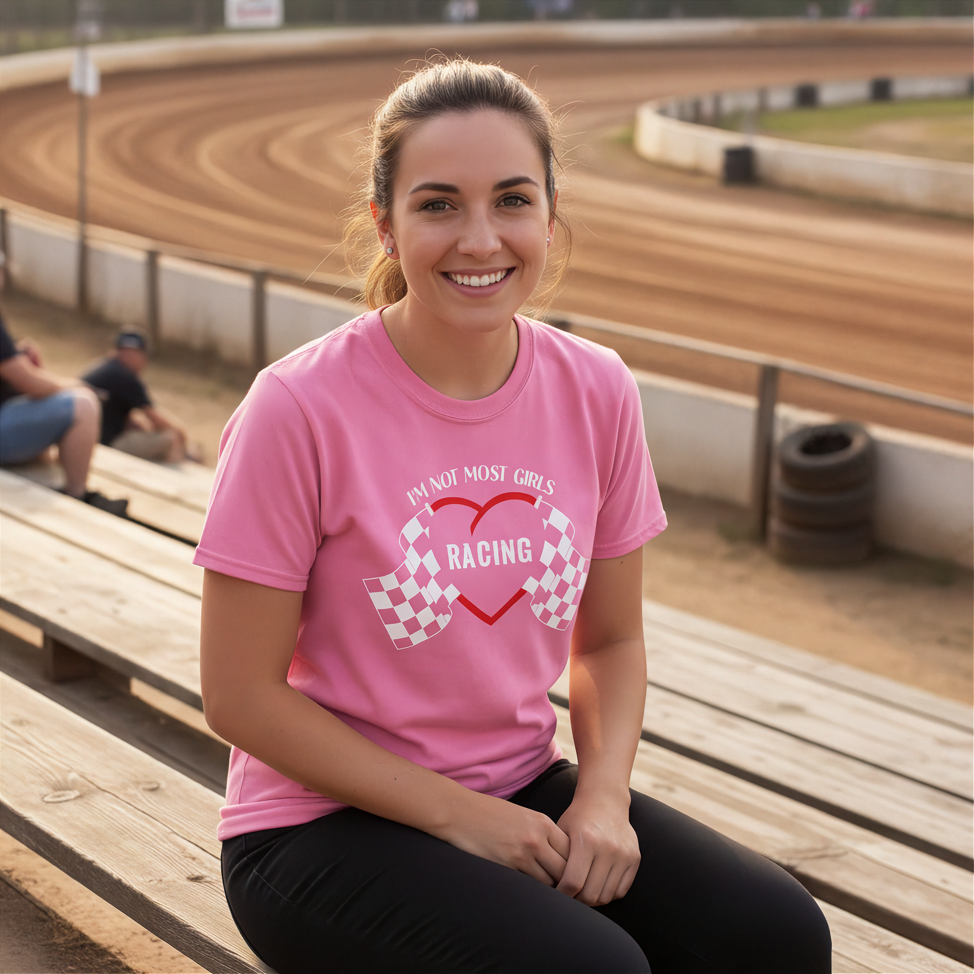 Woman wearing a pink t-shirt with racing design at a race track.
