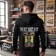 A man viewed from behind wearing a black hoodie with a large drag racing graphic and the text 'I'M NOT MOST MEN' on the back, standing in a garage-themed room with posters and shelves in the background.